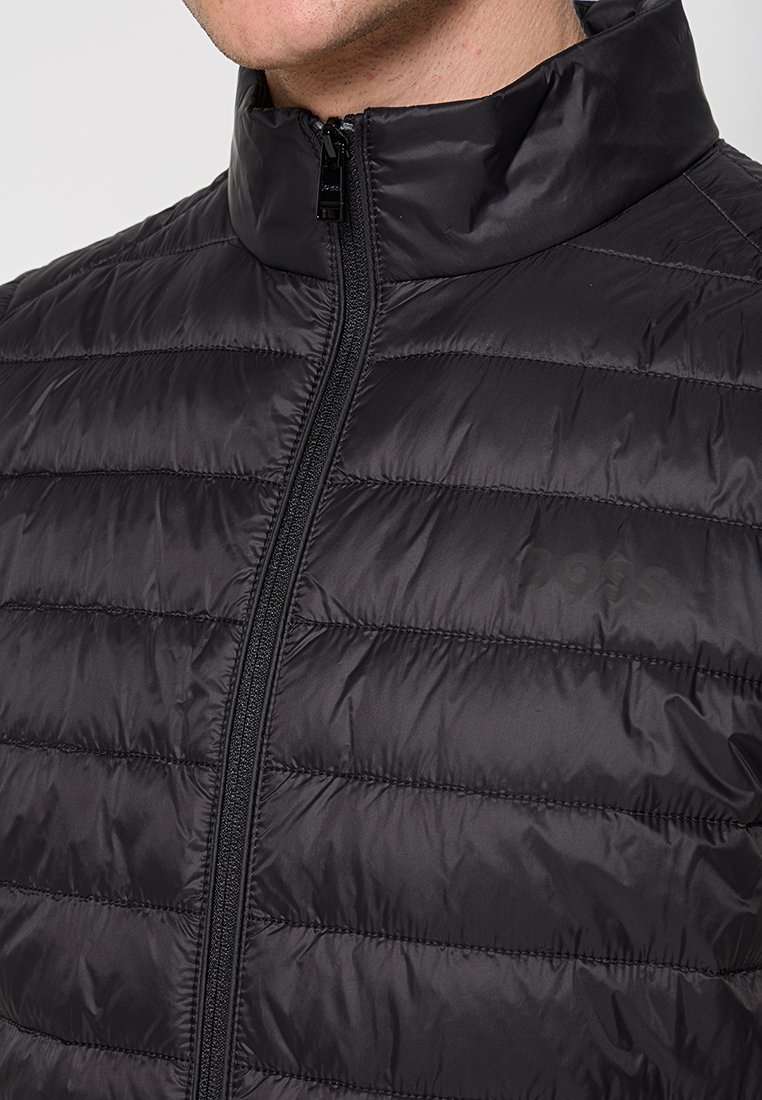 Giacca a vento nera con cuciture orizzontali, colletto alto e zip frontale. Include un marchio discreto nell'area del petto. Texture liscia.