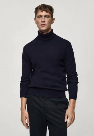 Knit turtleneck sweater in dark navy, featuring ribbed cuffs and hem, made from soft textured fabric, paired with dark trousers.