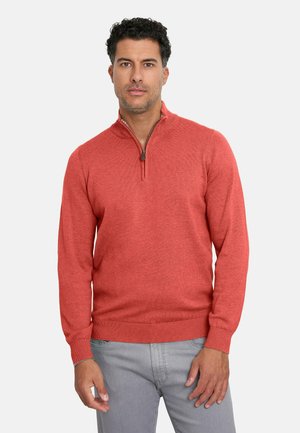 Suéter rojo de punto con cremallera de cuarto, hecho de una tela de punto texturizada. Presenta un cuello y dobladillo acanalados, combinado con jeans grises.