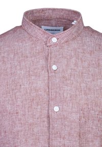 Camicia a maniche corte, con bottoni, realizzata in un tessuto leggero e testurizzato di un colore rosa tenue. Presenta un colletto rialzato e una tasca sul petto.