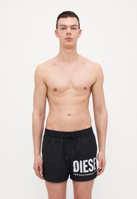 Shorts de bain noirs avec une ceinture élastique et un cordon de serrage, arborant un grand logo et texte "DIESEL" en blanc, fabriqués à partir d'un matériau léger et à séchage rapide.
