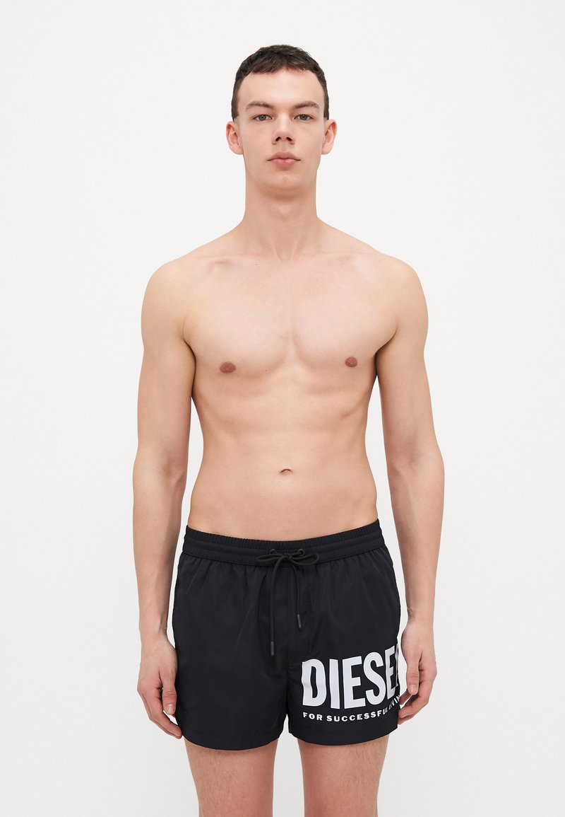 Shorts de bain noirs avec une ceinture élastique et un cordon de serrage, arborant un grand logo et texte "DIESEL" en blanc, fabriqués à partir d'un matériau léger et à séchage rapide.