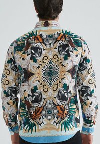 Homme portant une chemise à manches longues colorée avec des têtes de tigre symétriques, des lys blancs, des feuilles vertes et des motifs dorés ornés dans le dos.