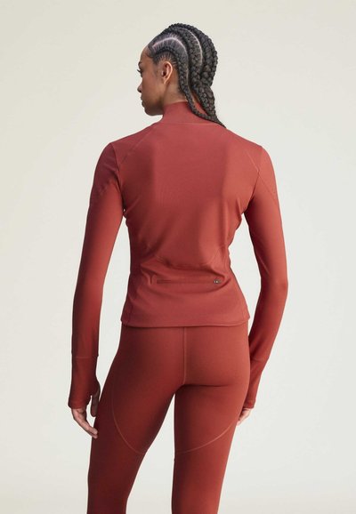 Langærmet atletiktop i rustrød, lavet af glat, strækbart stof. Har en høj krave og en lynlåslomme bagpå til praktisk brug.