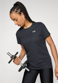 Sort ribbet atletisk t-shirt med et lille hvidt logo, båret af en person der holder en vægt, kombineret med sorte leggings.