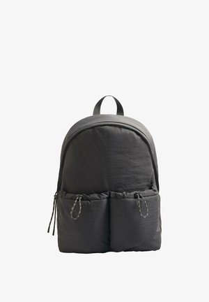 Czarny plecak o zaokrąglonym kształcie, wykonany z teksturowanej tkaniny. Posiada uchwyt na górze oraz dwie przednie kieszenie z zaciąganymi trokami.