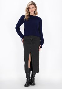 Navy Pullover mit langen Ärmeln und rundem Ausschnitt, kombiniert mit einem schwarzen Jeansrock mit Schlitz vorne und schwarzen kniehohen Stiefeln.