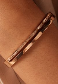 Roze gouden armband met een strak, rechthoekig ontwerp en een gestructureerde rand, verfraaid met een rij kleine ingelegde kristallen voor visuele detail.