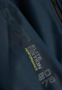 Granatowy materiał z napisem „SPEC. ELITE EDITION PERFORMANCE” w szaro-żółtej kolorystyce; posiada gładką teksturę i szczegół z suwakiem.