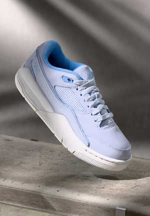 Jasnoniebieski sneaker z teksturowaną podeszwą i sznurowadłami, ustawiony nad betonową powierzchnią z miękkim cieniem w tle.