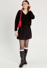 Black knitted sweater with a V-neck, paired with a black flowy skirt. Knee-high black boots with white accents and a red crossbody bag.