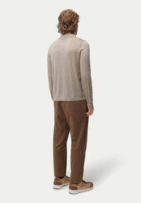 Beige långärmad topp med krage, i kombination med bruna byxor och bruna och gula sneakers. Slät textur med en avslappnad passform.