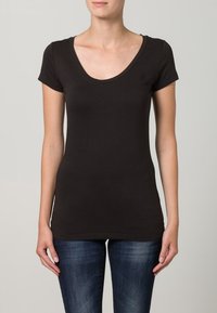 Svart slim fit t-shirt i mjuk bomull med rundad hals och korta ärmar. Noterbar liten logotyp på vänster bröst. Parat med blå denimjeans.