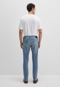 Hellblaue Jeans in Slim Fit mit Gesäßtaschen und einem schwarzen Etikett am Taillenbund, kombiniert mit einem schlichten weißen T-Shirt.
