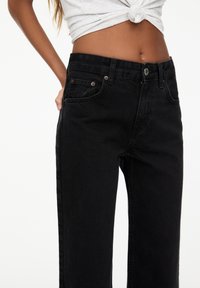 Zwarte high-waisted denim jeans met een rechte pasvorm, voorzien van voorzakken en subtiele koperen details bij de taille.
