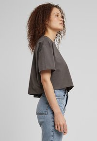 Harmaa lyhythihainen crop-top, jossa on pyöreä kaula-aukko ja rento istuvuus, yhdistettynä vaaleansinisiin korkeavyötäröisiin farkkuihin, joissa farkkutehoste on näkyvissä.