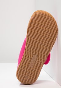 Różowa cholewka buta o miękkiej fakturze, z gumową podeszwą o poziomych rowkach i widoczną wytłoczoną metką z logo.