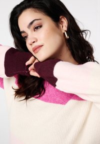 Grofgebreide trui in crème, roze en bordeauxrood. Heeft een kleurblokontwerp, geribde manchetten en een ontspannen pasvorm. Getextureerde, warme stof.