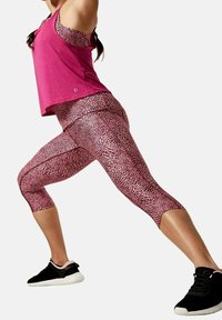 Lyserød sports-top med racerback-design, parret med capri leggings med et lyserødt og sort leopardmønster. Sorte træningssko fuldender outfittet.