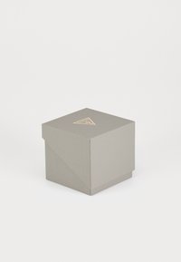 Szary kwadratowy box o teksturowanym wykończeniu, z złotym trójkątnym logo na górze oraz nachylonych bokach, co nadaje mu nowoczesny design.