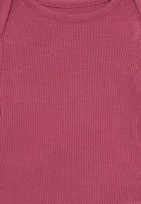 Weiches rosa Rippenstrickgewebe mit Rundhalsausschnitt und subtilem Texturmuster, das den oberen vorderen Bereich eines Kleidungsstücks zeigt.