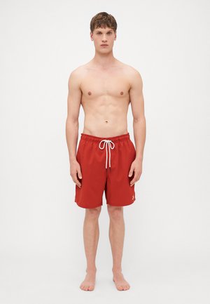Shorts de bain rouges en tissu léger avec une taille élastique, un cordon blanc, et un petit logo sur la jambe gauche.