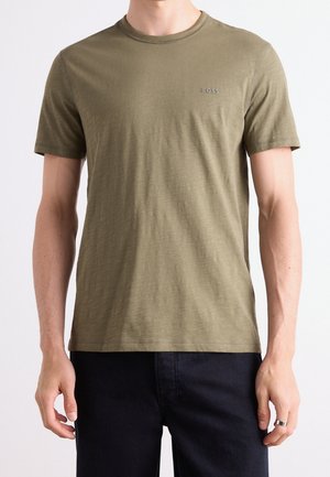 Mand iført en olivengrøn kortærmet BOSS t-shirt kombineret med sorte bukser, stående med armene afslappet ned langs siden.