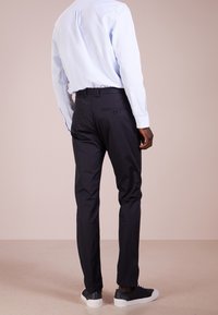 Donkerblauwe broek met een slim fit, voorzien van een gladde textuur, zijzakken en achterzakken met knopen. Gepaard met een lichtblauw shirt.