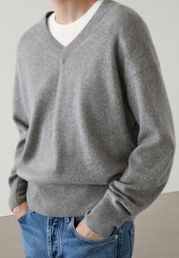 Gray wool v-neck sweater with a ribbed hem and cuffs, worn over a white t-shirt, paired with blue jeans. Smooth texture, relaxed fit.