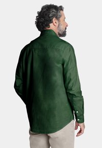 Camisa de manga larga de algodón en verde oscuro, con cuello y puños con botones, textura suave y dobladillo curvado. Vista trasera mostrada.