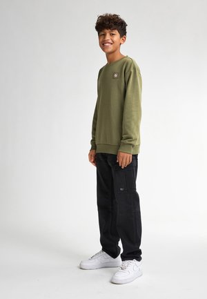 Olijfgroene sweatshirt met ronde hals en logopatch, gecombineerd met zwarte cargo pants met zakken. Witte sneakers maken de look af.