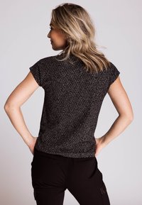 Schwarz-weiß gemustertes kurzärmeliges Oberteil mit lockerem Sitz und einer dezenten Struktur. Modell von hinten gezeigt, mit offenem Haar.