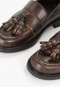 Mocassini in pelle marrone con decorative nappine, dotati di più occhielli e design a punta tonda. Suola in gomma nera con un leggero tacco.