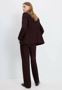 Bordeauxrød skræddersyet dragt med en struktureret blazer og lige bukser, der har knapdetaljer og en glat tekstur.