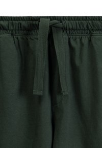 Ciemnozielone dresy z elastycznym paskiem w talii i sznurkiem. Miękki materiał o gładkiej teksturze, z kieszenią po bokach.