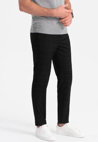 Pantalon slim à motifs carreaux noirs en tissu extensible, associé à des sneakers blanches. La tenue est complétée par un haut gris clair.