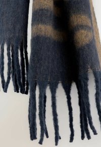 Wełniany szalik w ciemnoniebieskim kolorze z brązowymi wzorami, charakteryzujący się długimi, nierównymi frędzlami wzdłuż brzegów oraz miękkim, teksturowanym materiałem.