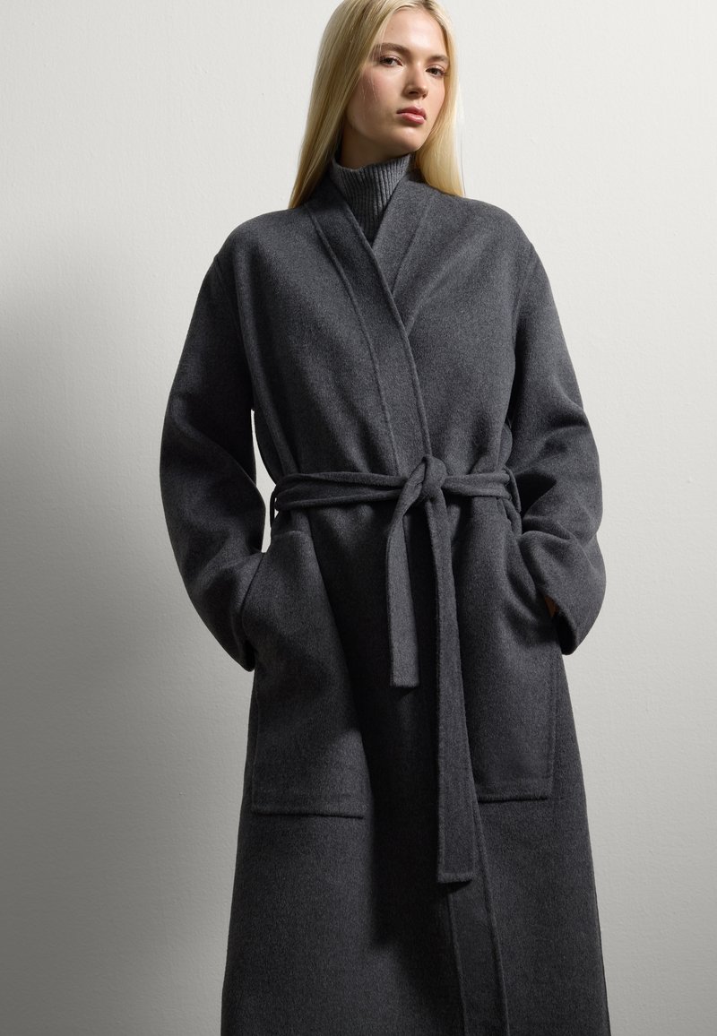 Cappotto avvolgente grigio in lana con cintura, tasche profonde e colletto a scialle. Tessuto testurizzato con una finitura morbida. Maniche lunghe e vestibilità rilassata.