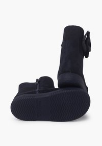 Botas de ante azul marino hasta el tobillo con una parte superior curva, cremallera lateral y un lazo decorativo. La suela de goma gruesa presenta un patrón de tracción en zigzag.