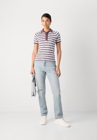 Gestreepte poloshirt in wit en kastanjebruin, met een kraag en drie knopen. Gecombineerd met lichtblauwe distressed jeans en witte sneakers, met een zilveren tas in de hand.