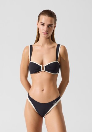 Sort bikini sæt med tykke stropper og cremefarvede accenter. Toppen har et snøret design i midten og en lukning foran. Glat tekstur.