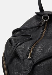 Gros plan d’un sac en cuir noir texturé avec une fermeture éclair dorée et une languette de tirette sur un fond blanc.