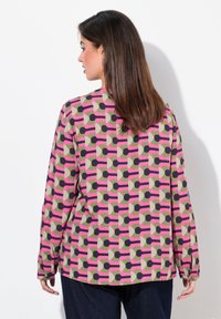Camicetta a maniche lunghe in tessuto testurizzato con un motivo geometrico. Colori includono rosa, verde e blu scuro. Vestibilità leggermente rilassata.
