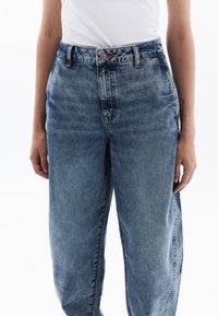 Džíny s vysokým pasem v světlé modré barvě, s volným střihem, vybledlým vzhledem a zapínáním na knoflík. Obsahují postranní kapsy a poutka na opasek.