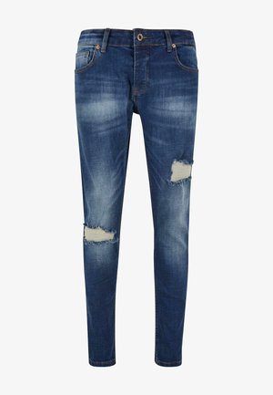 Vékony kék farmernadrág, elhalványult területekkel és két térdgumival. Gombos és cipzáras záródás, övhurkok és elülső zsebek jellemzik.