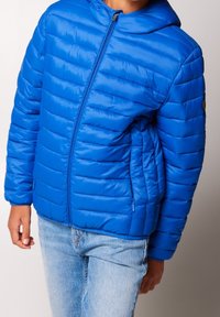 Chaqueta acolchada azul con capucha, que presenta un acolchado horizontal, cremallera frontal y bolsillos laterales. Textura suave y brillante, y diseño ligero.