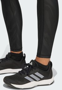 Schwarze Sportleggings mit einem dezenten Muster, kombiniert mit schwarz-grauen Sportschuhen, die drei Streifen und ein strukturiertes Strickobermaterial aufweisen.