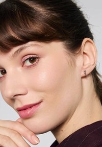 Srebrny nausznik w kształcie kolczyka z małymi czarnymi koralikami, zakrzywiony design. Modelka ma jasnobrązowe włosy, brązowe oczy i neutralny makijaż.