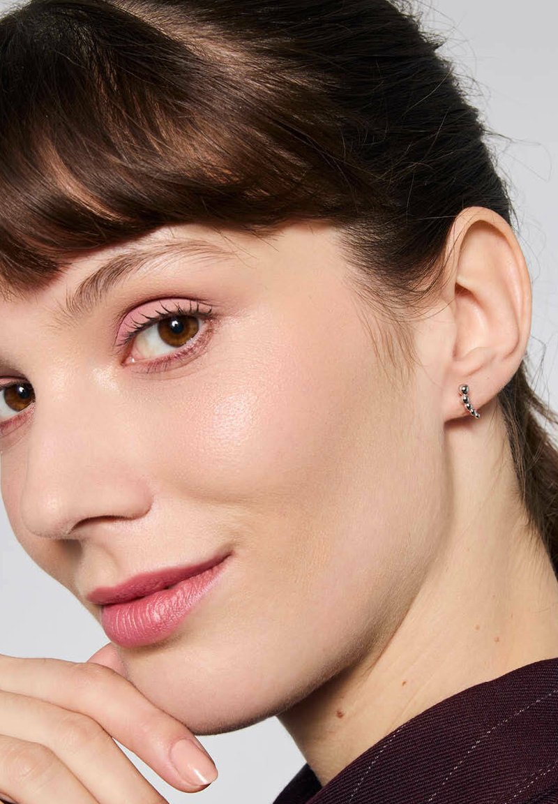 Srebrny nausznik w kształcie kolczyka z małymi czarnymi koralikami, zakrzywiony design. Modelka ma jasnobrązowe włosy, brązowe oczy i neutralny makijaż.