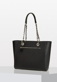 Sac fourre-tout en cuir noir avec poignées en chaîne argentée et une poche zippée à l'avant, posé sur une surface blanche devant un fond blanc.